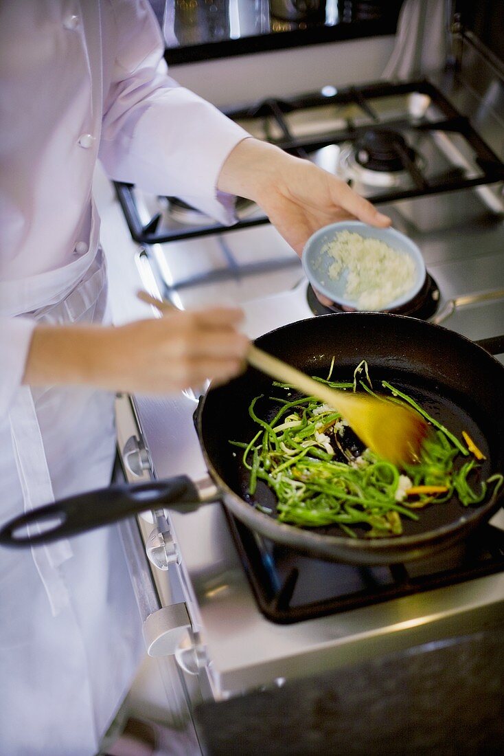 Female chef sautéing green beans with onions