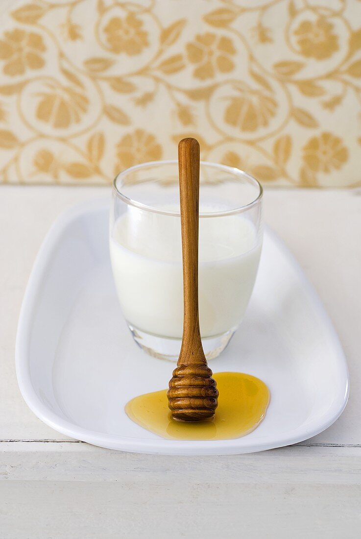 Glass of milk with honey dipper
