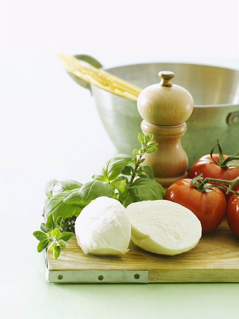 Tomatoes, basil, mozzarella on chopping board, spaghetti in pan