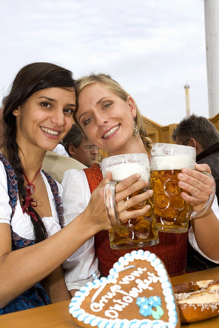 Zwei Frauen mit vollen Bierkrügen beim Anstossen (Oktoberfest)