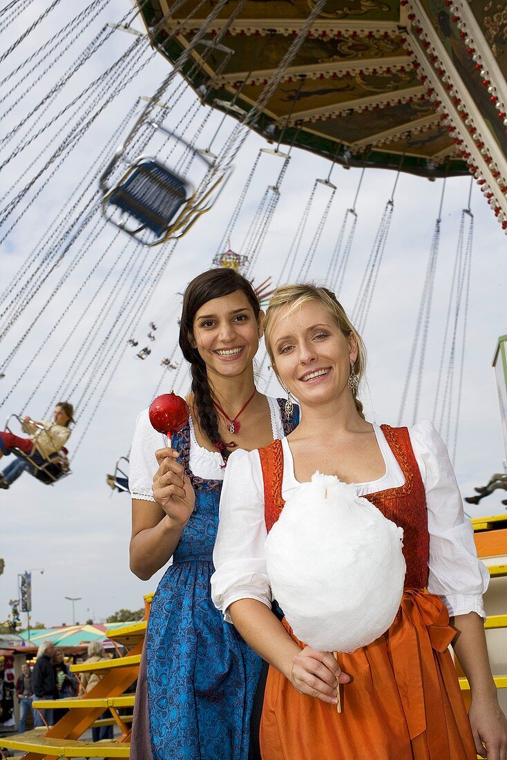 Zwei Frauen mit Liebesapfel und Zuckerwatte vor Kettenkarussell (Oktoberfest)