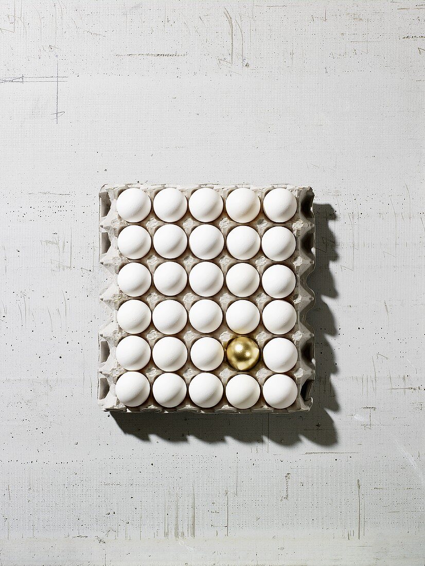 White eggs and one golden egg in an egg tray