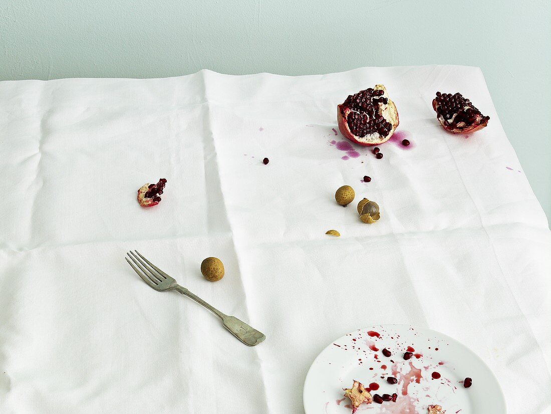 Pomegranate, lychee and plate on dirty tablecloth