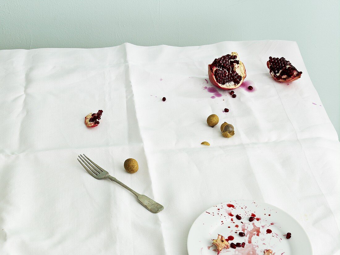 Schmutzige Tischdecke mit Granatapfel, Litchi und Teller