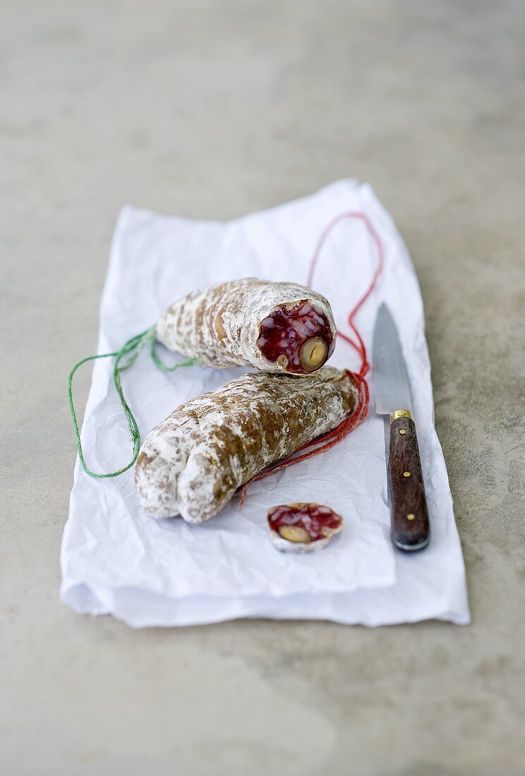 Hard cured sausage with nuts on paper with a knife