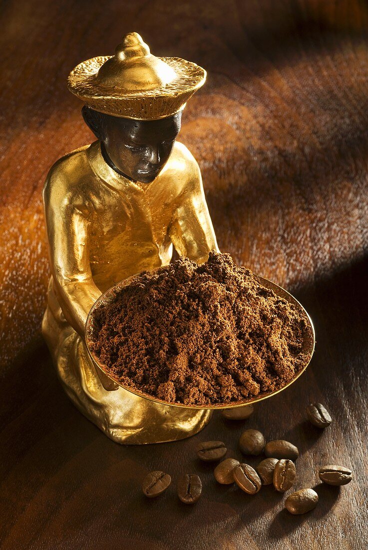 Gilded statuette with a bowl of ground coffee, coffee beans