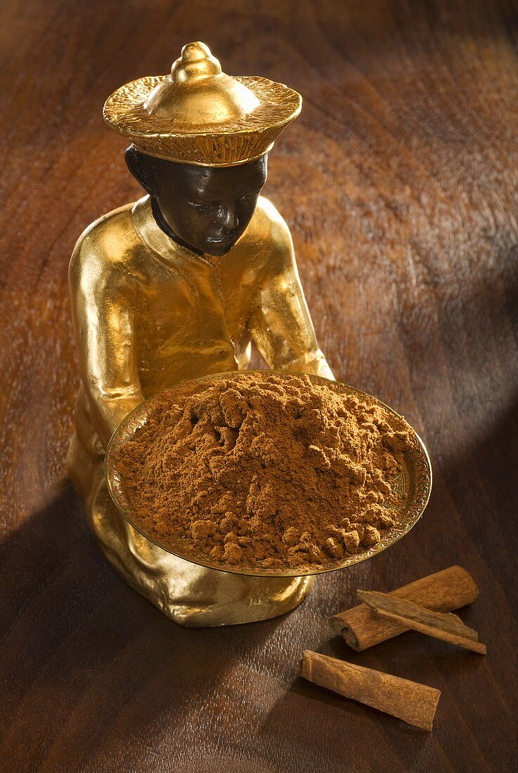 Gilded statuette with bowl of ground cinnamon, cinnamon bark