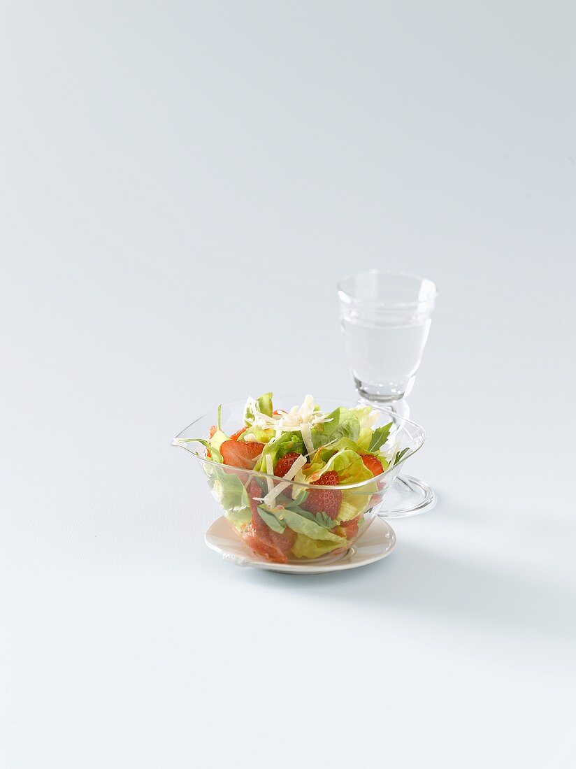 Blattsalat mit Erdbeeren und Parmesan, ein Glas Wasser