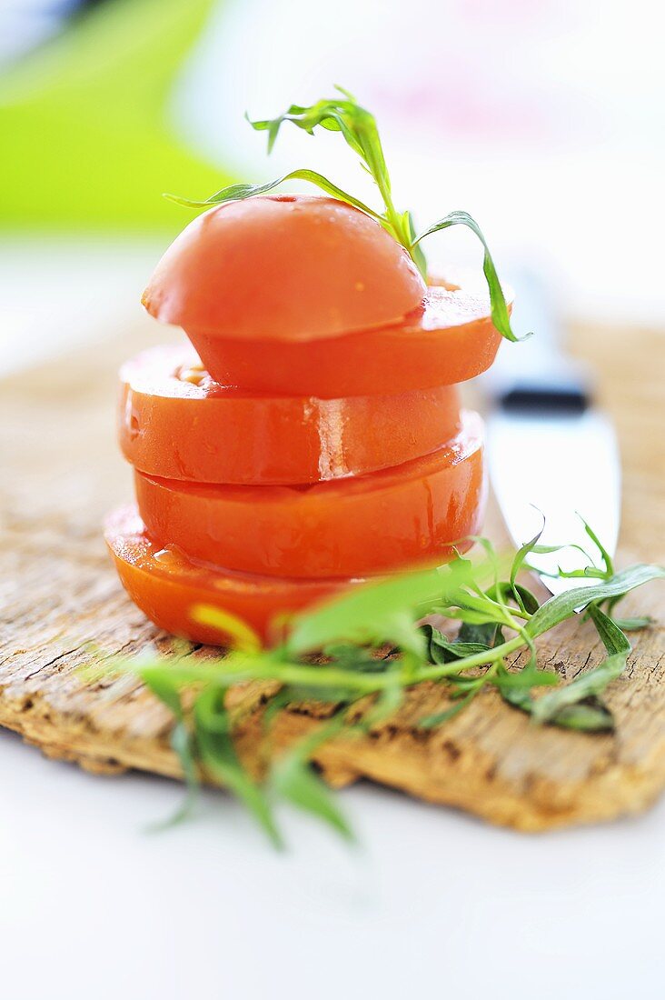 Tower of tomato slices with tarragon on a wooden board
