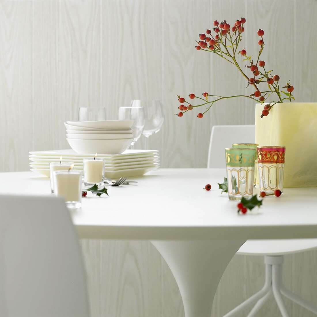 Gedeckter Tisch mit weißem Geschirr, Gläsern, Kerzen, Hagebutten und Ilex