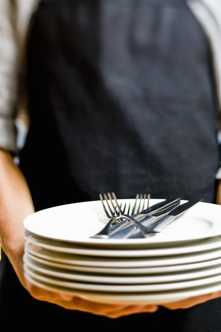 Person holding pile of plates with cutlery