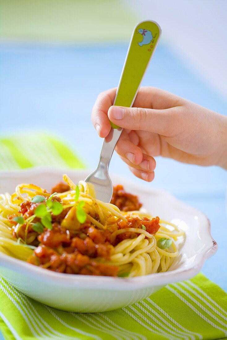 Kinderhand dreht Spaghetti Bolognese auf eine Gabel