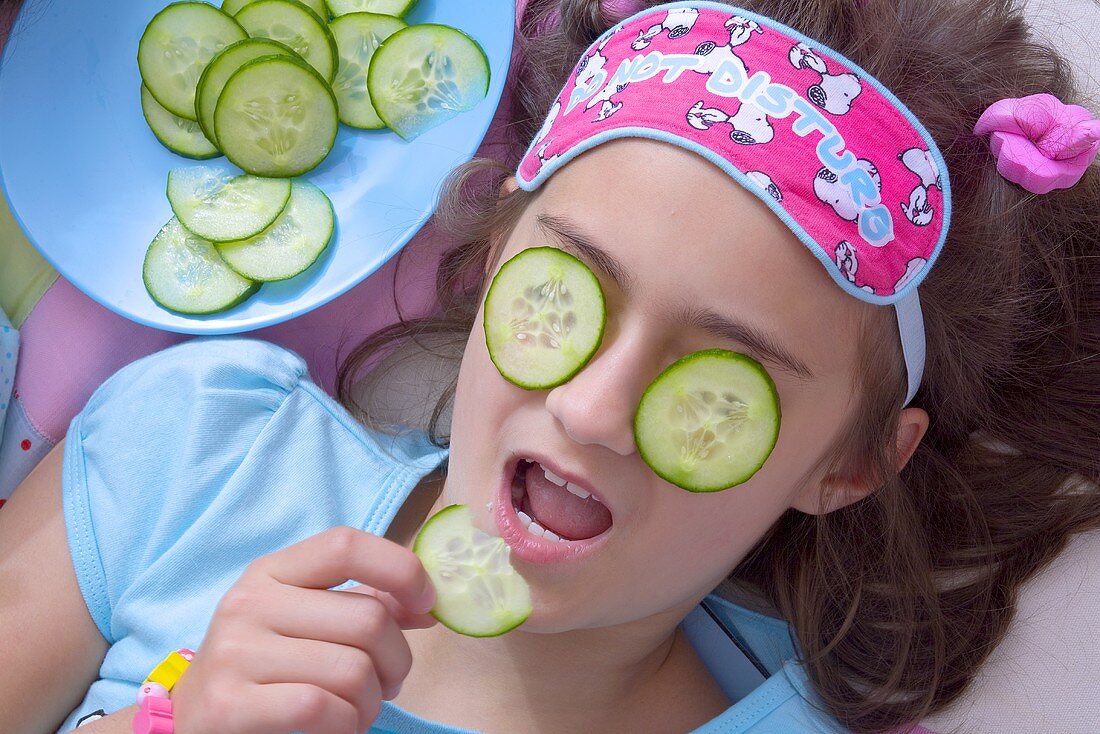 Mädchen mit Gurkenmaske isst Gurkenscheibe