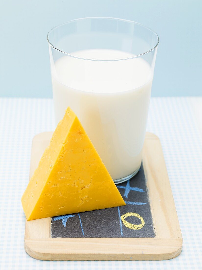 Glass of milk and piece of Cheddar cheese on slate board