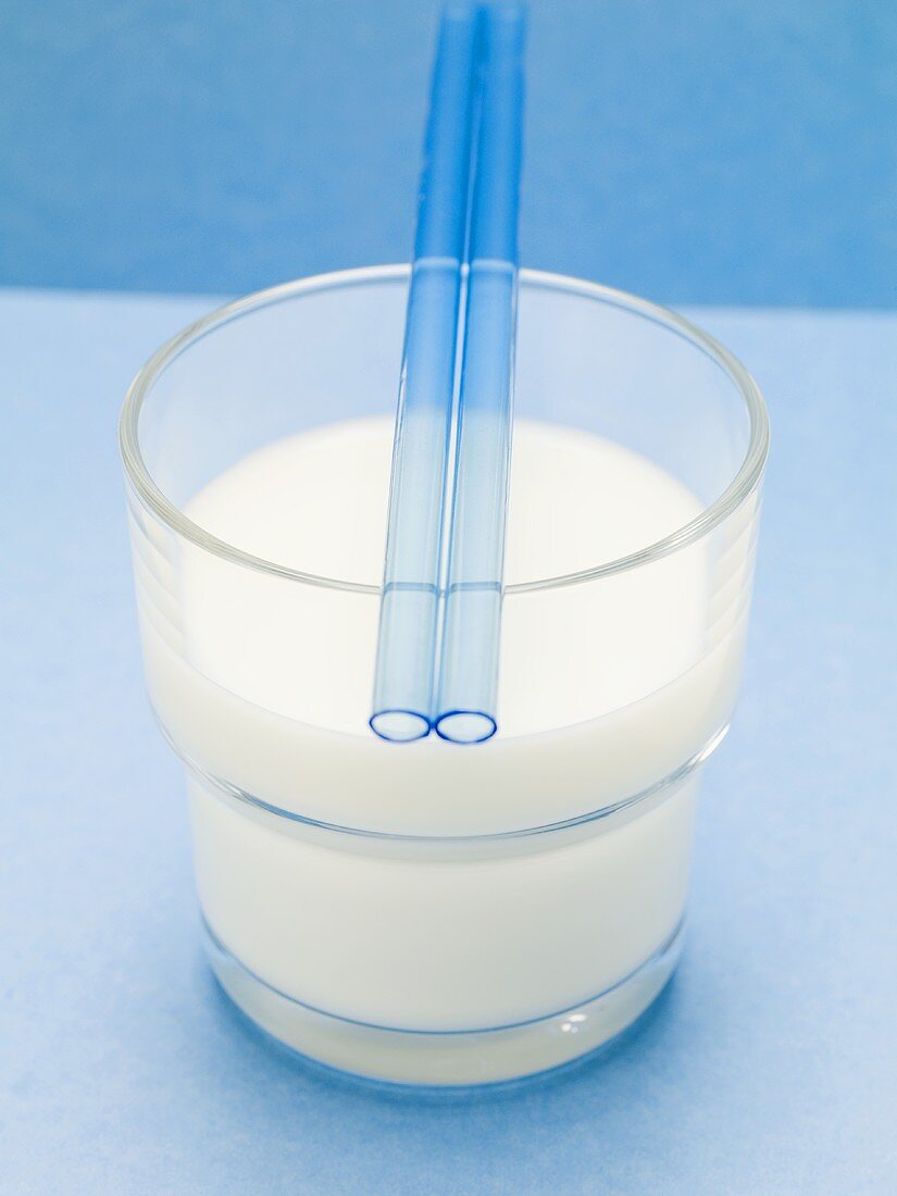 Blaue Strohhalme auf Glas Milch