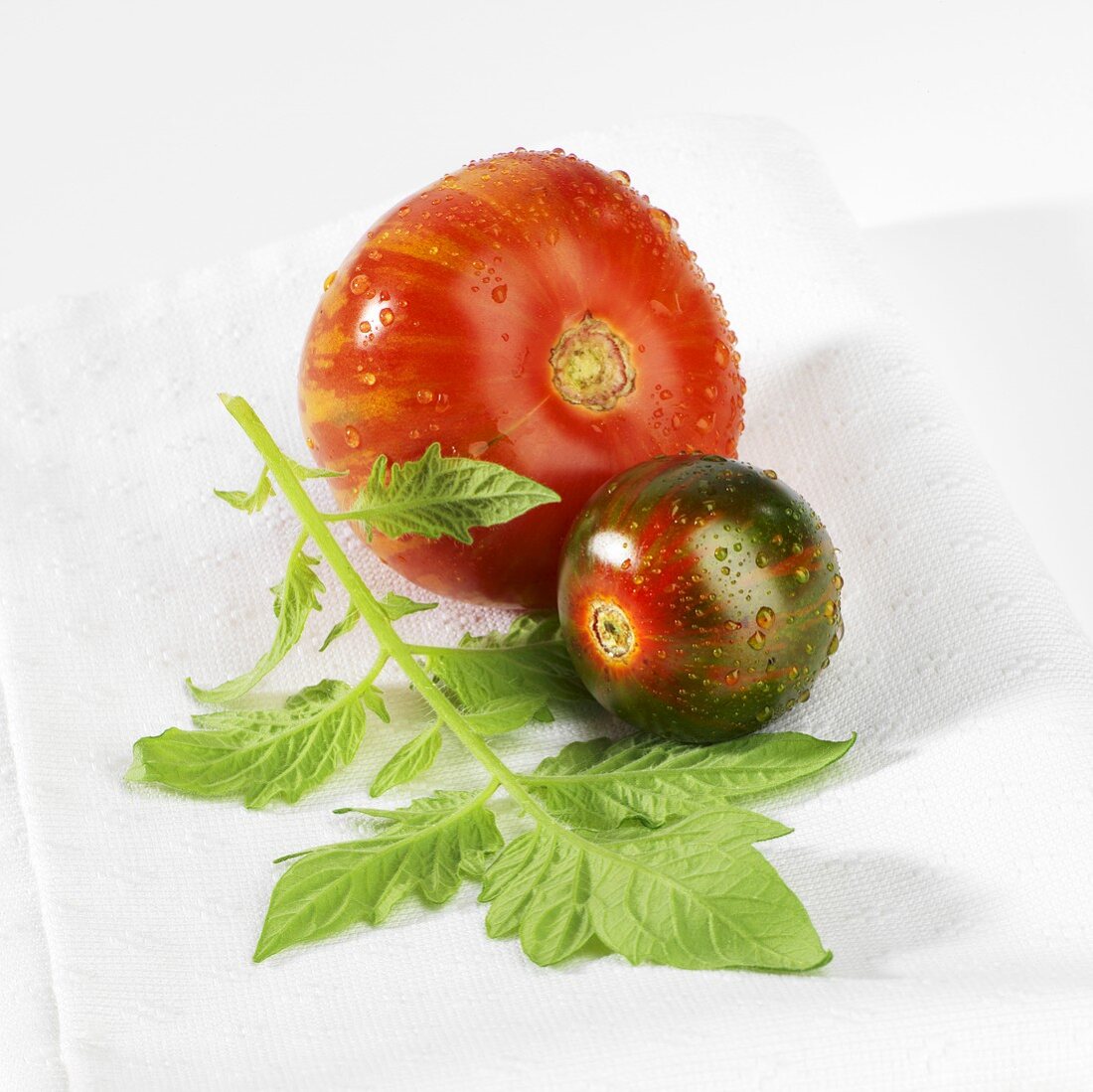 Two tomatoes with drops of water and leaf