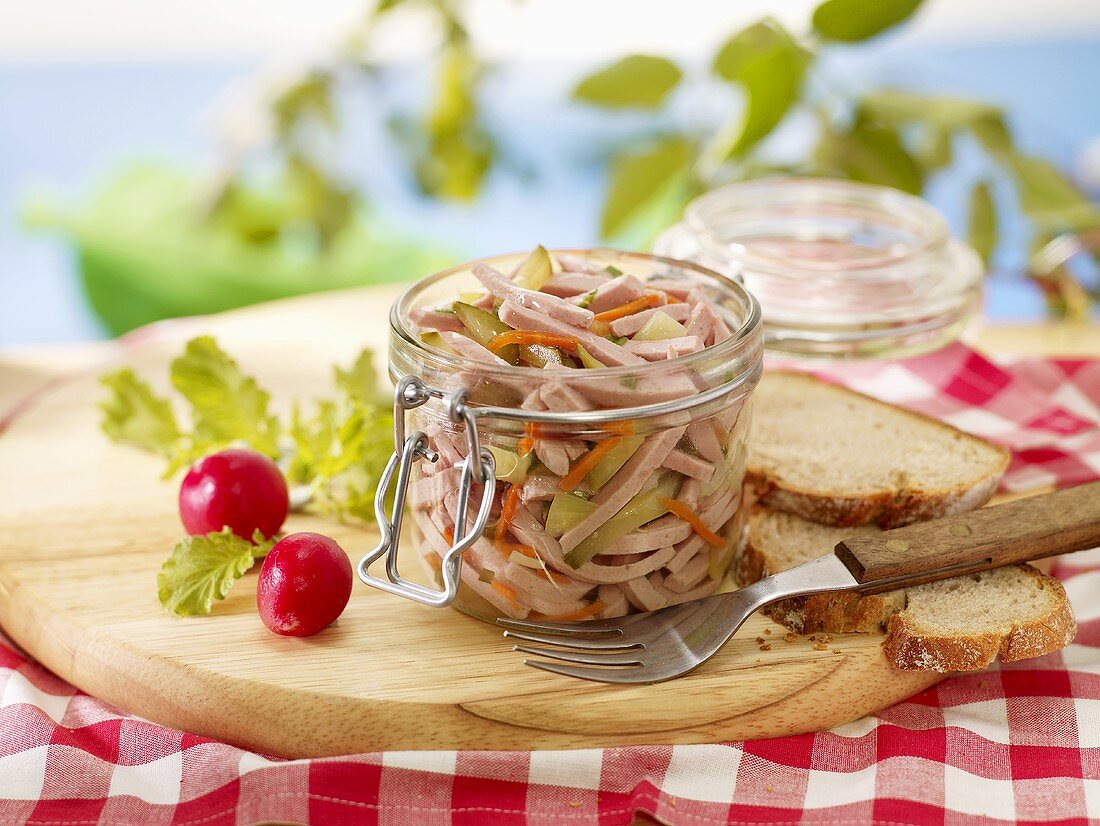 Sausage salad in a preserving jar with bread and radishes