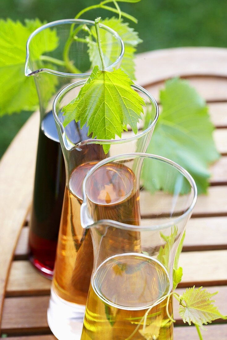 Weißwein und Rotwein in Karaffen auf Holztisch im Freien