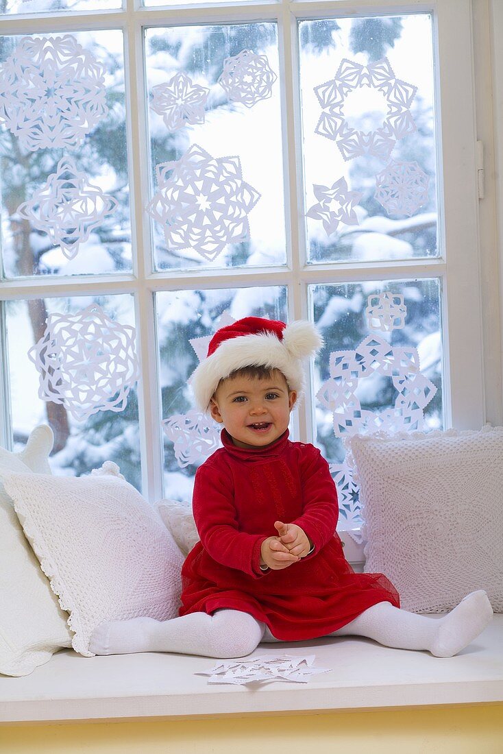 Little girl in Santa costume sitting by window