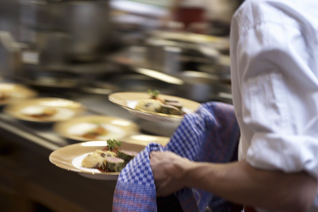 Waiter carrying plates of food in a professional kitchen