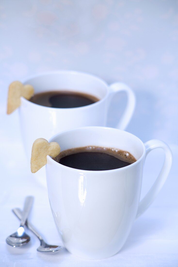 Two cups of black coffee with heart-shaped biscuits