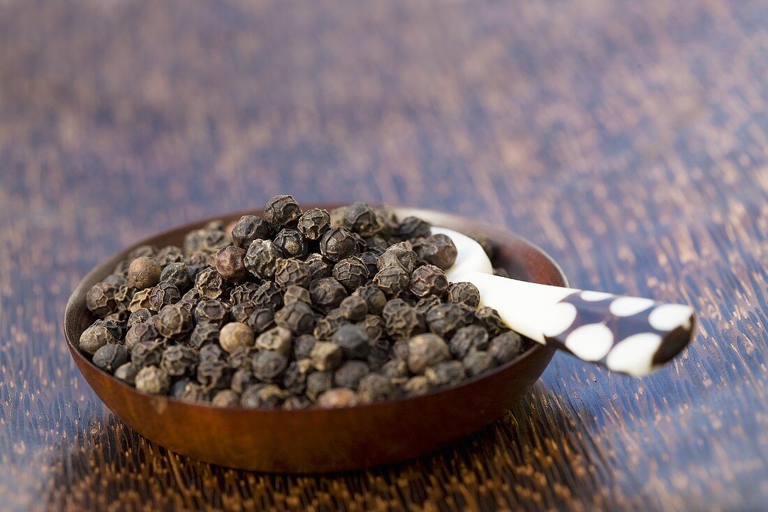 Black peppercorns in a small wooden dish with spoon