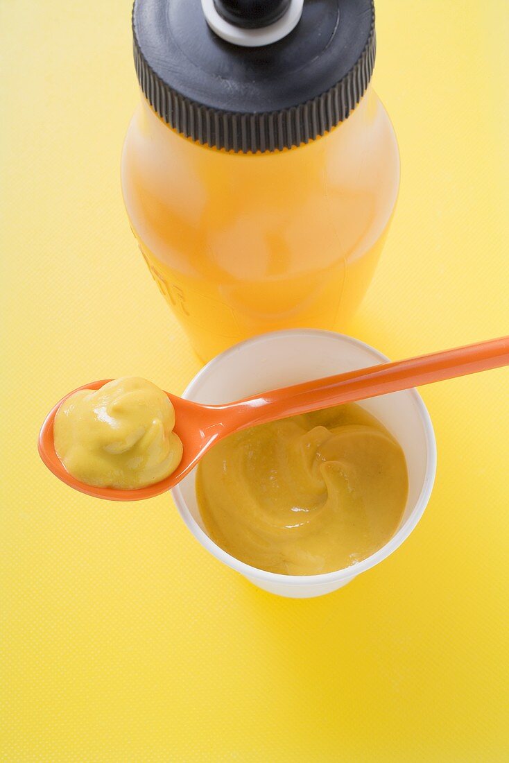 Mustard in plastic pot and on plastic spoon