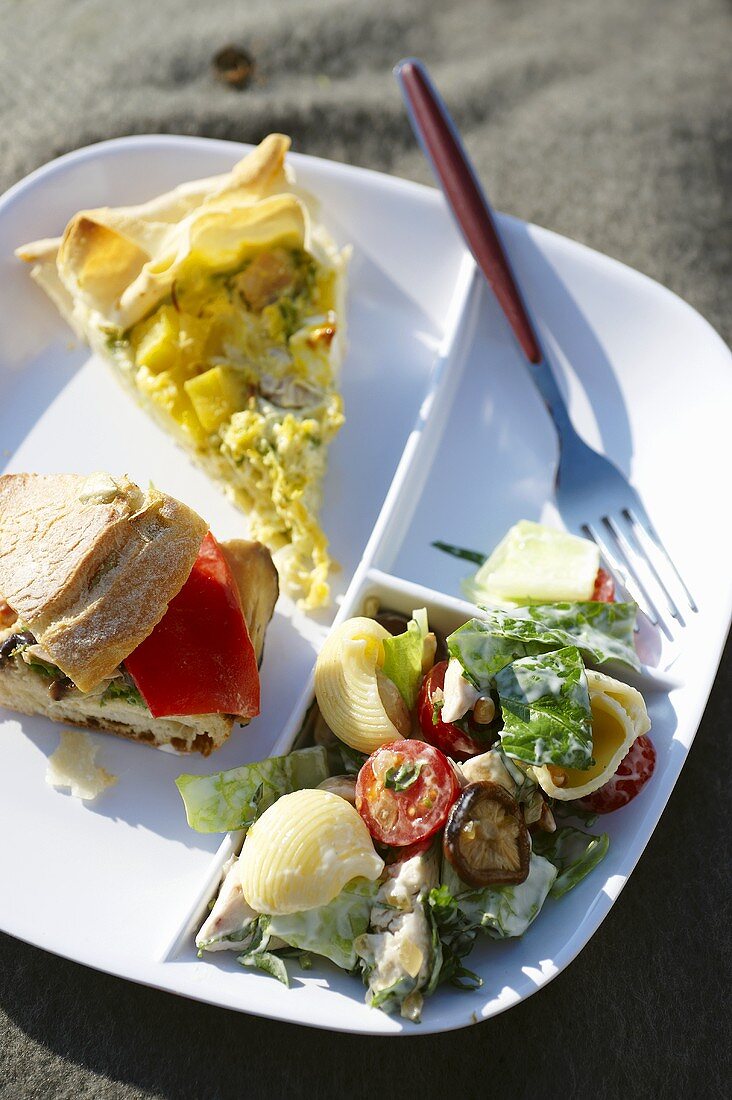 Quiche, Sandwich und Nudelsalat auf einem Picknickteller