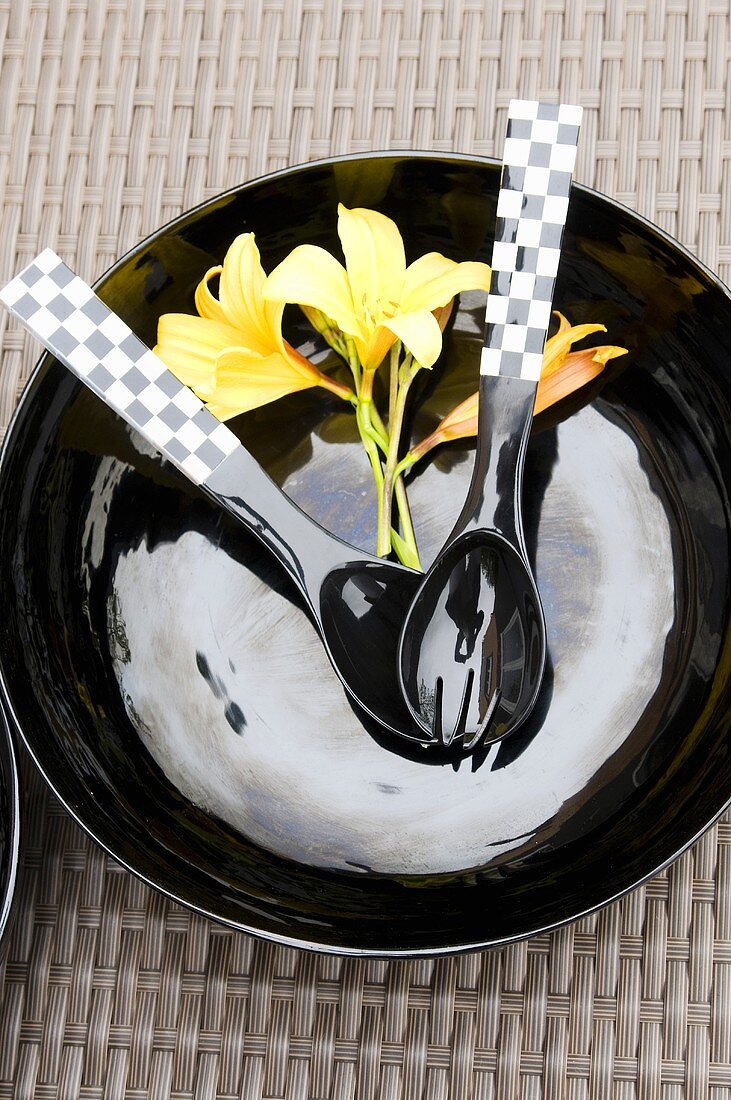 Schwarzes Teller mit Besteck und gelben Blüten