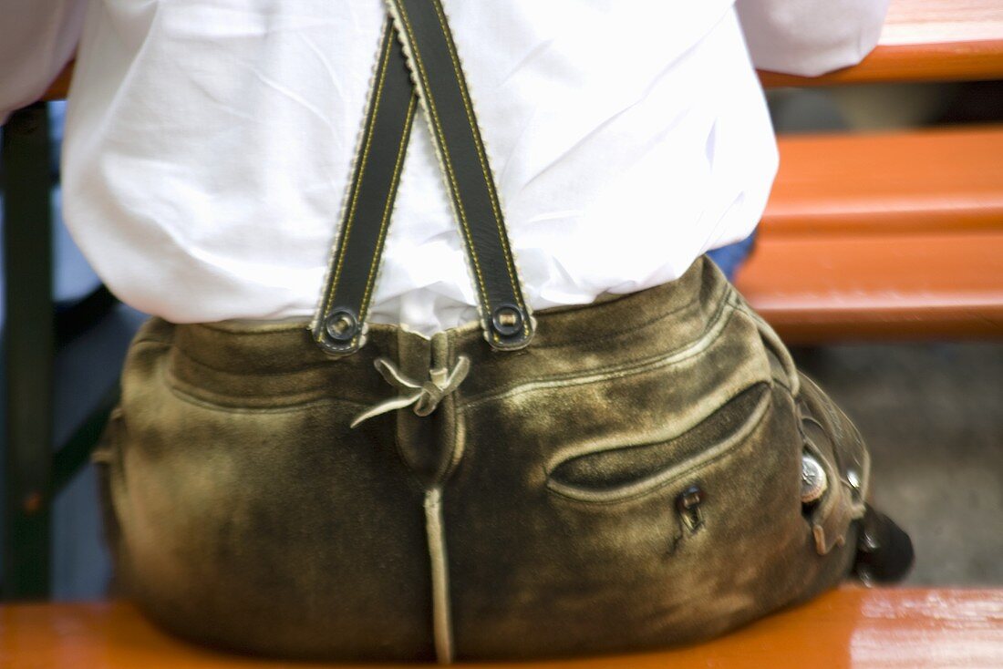 Mann mit Lederhose sitzt auf einer Bierbank