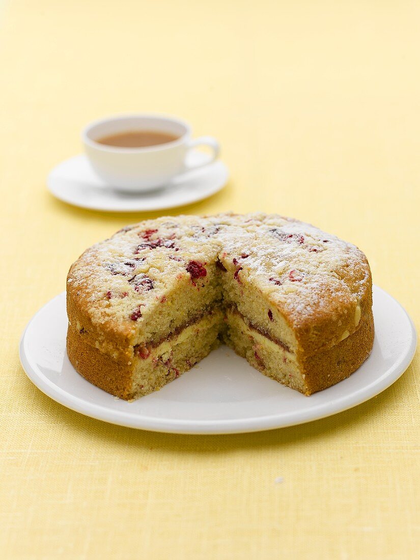 Raspberry sponge cake, a piece removed, cup of tea