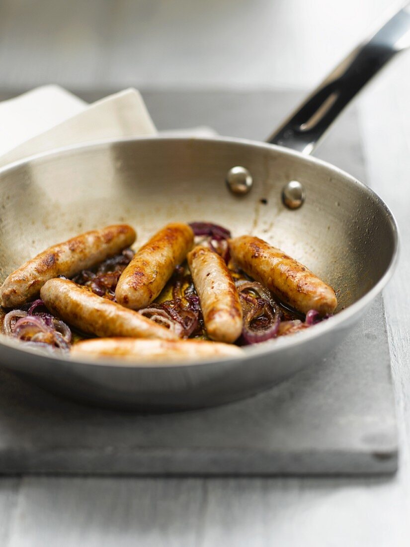 Chipolatas and onions in a frying pan