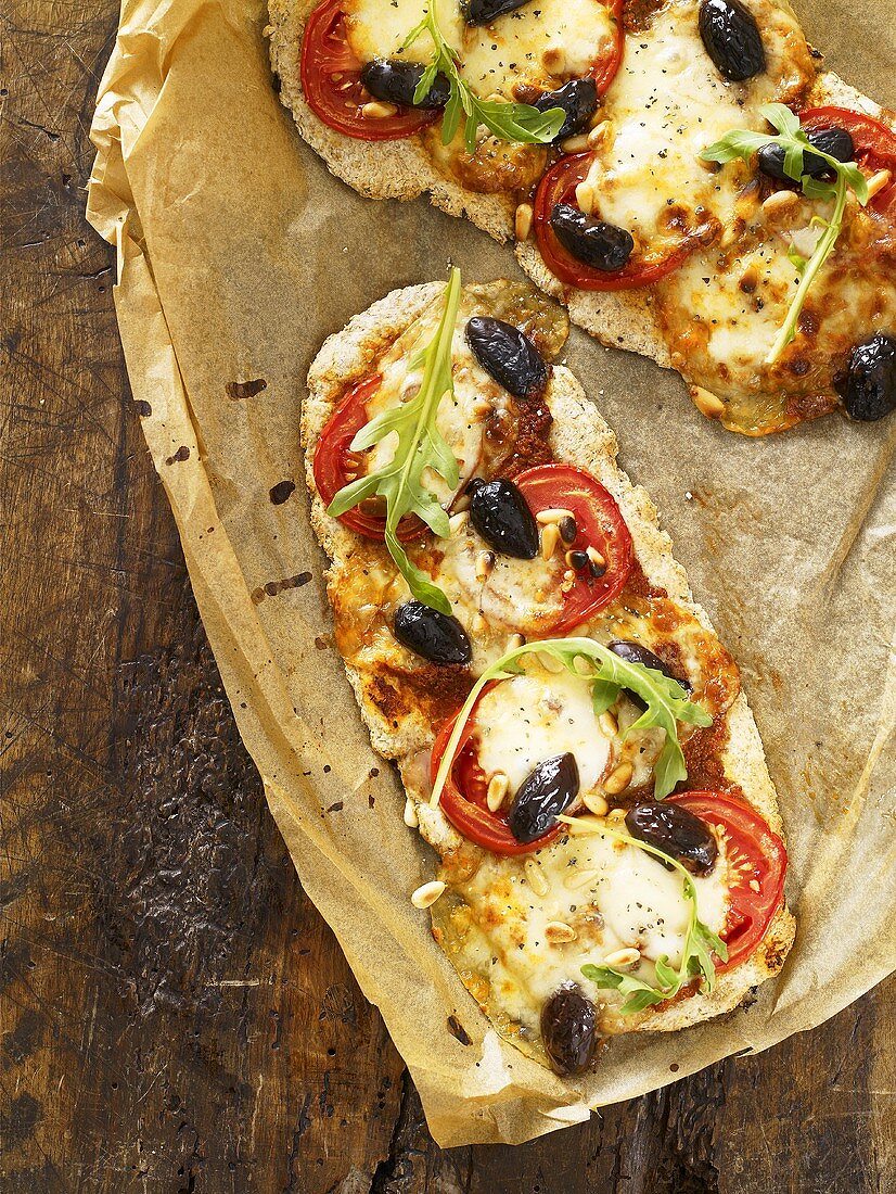 Cheese and tomato pizzas with olives & rocket on baking parchment