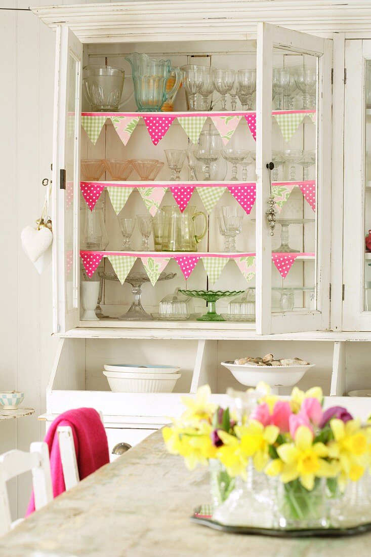 Cupboard full of glasses, narcissi on table