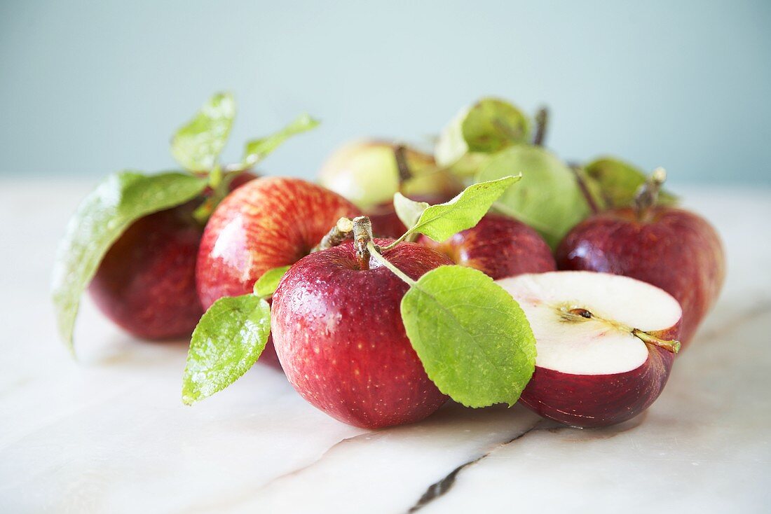 Mehrere ganze und ein halber roter Apfel mit Blättern