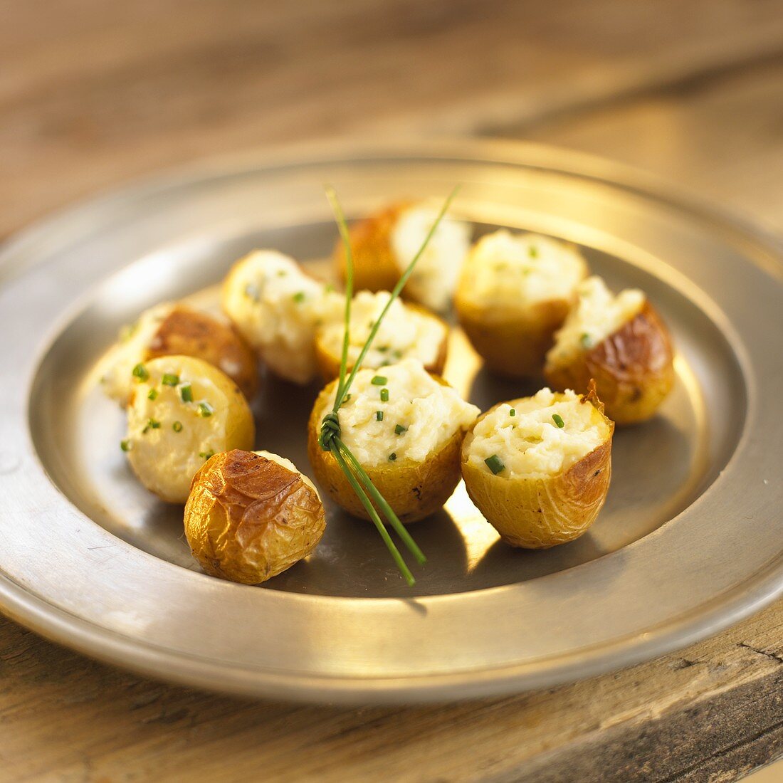 Small baked potatoes with chives on pewter plate