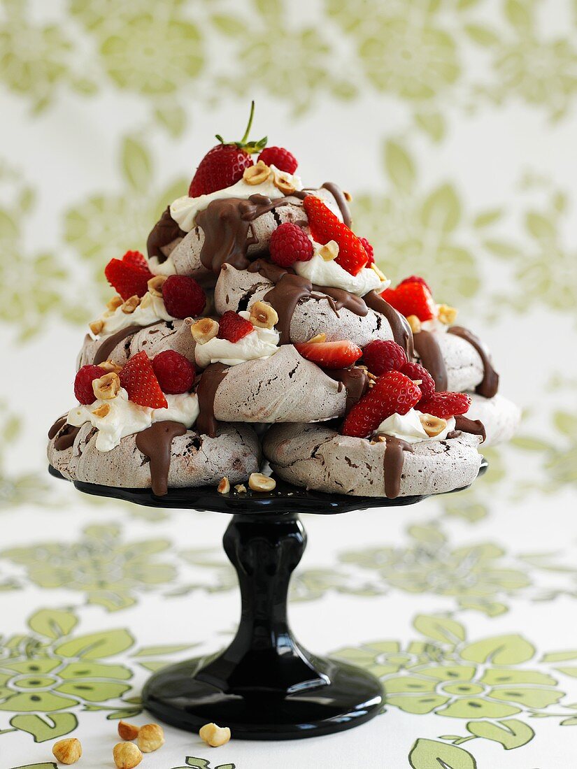 Meringues with chocolate sauce, berries, cream & nuts on cake stand