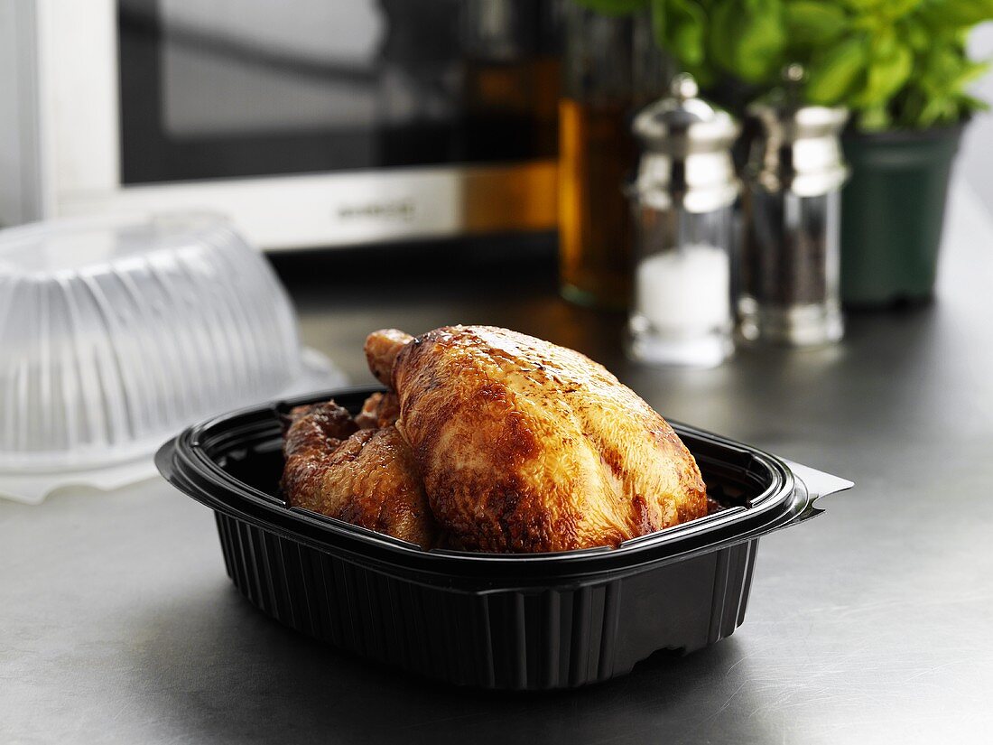 Take-away roast chicken in plastic container in front of microwave