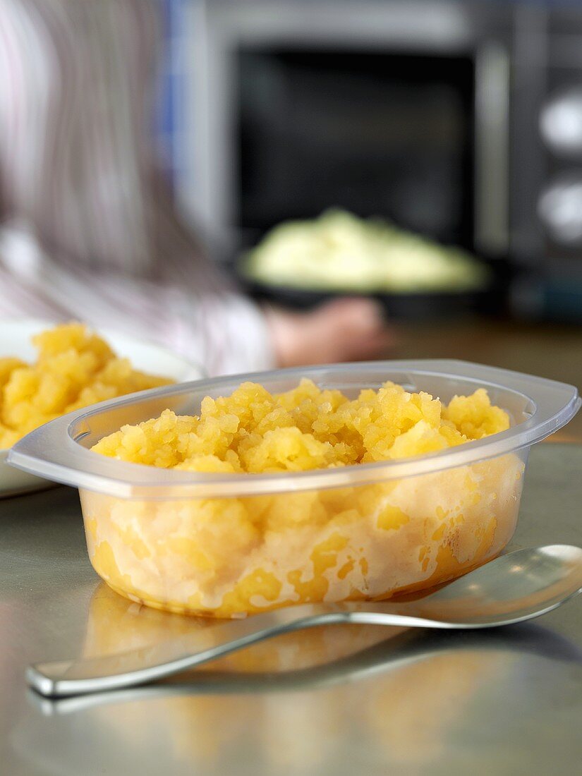 Vegetable puree in plastic container in front of microwave oven