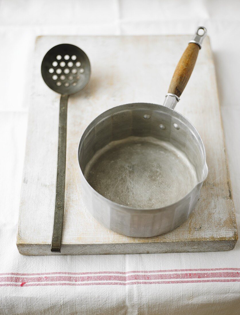 Saucepan and slotted spoon on a wooden board