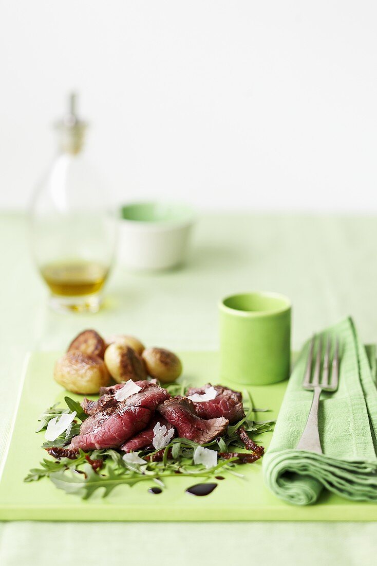 Sliced roast beef on rocket with parmesan, baked potatoes