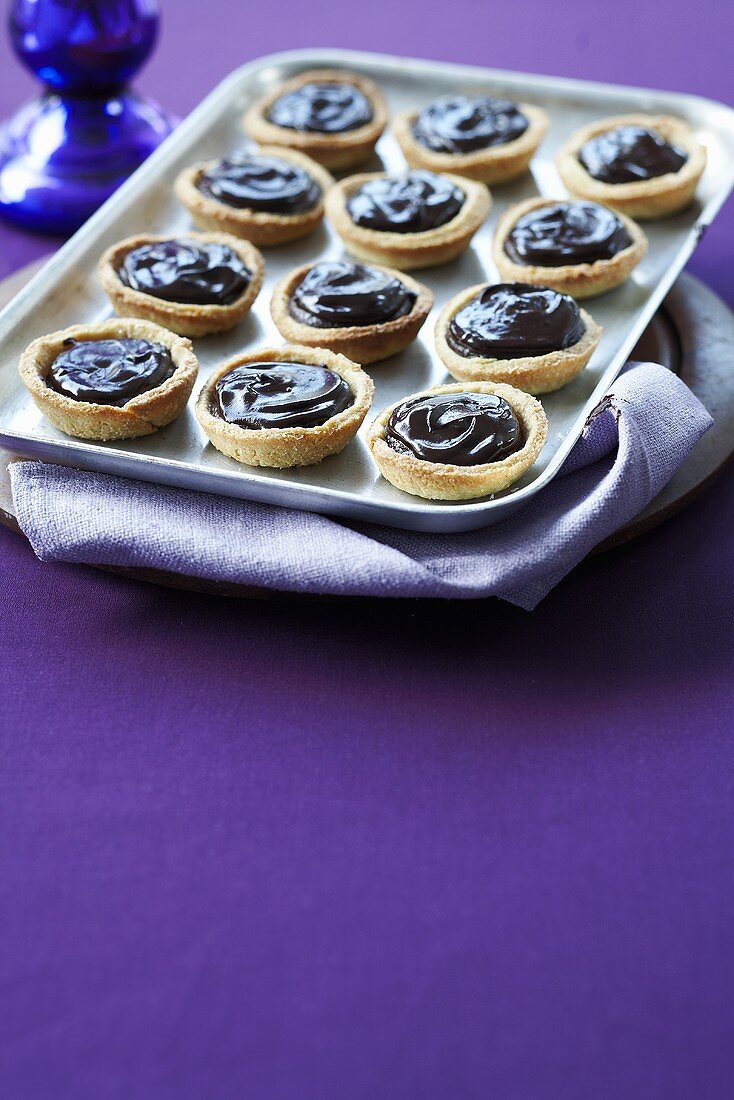 Twelve chocolate tartlets on a tray