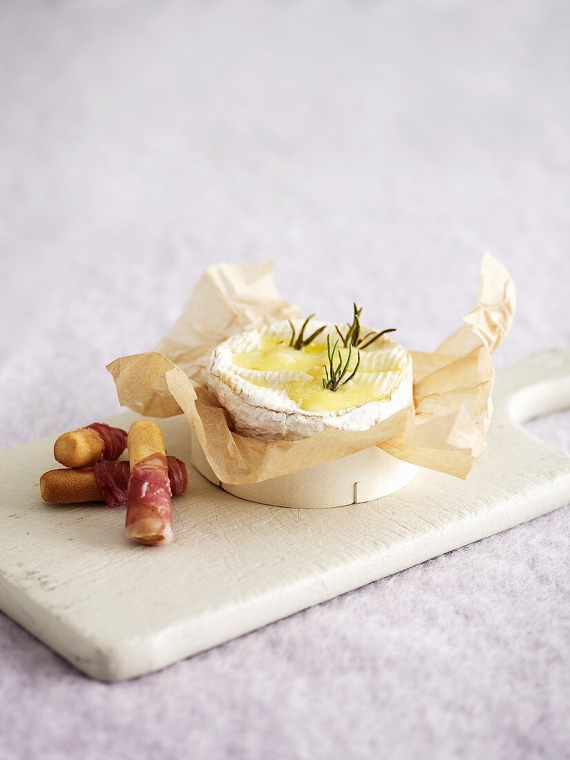 Cheese baked in wooden box, ham-wrapped grissini