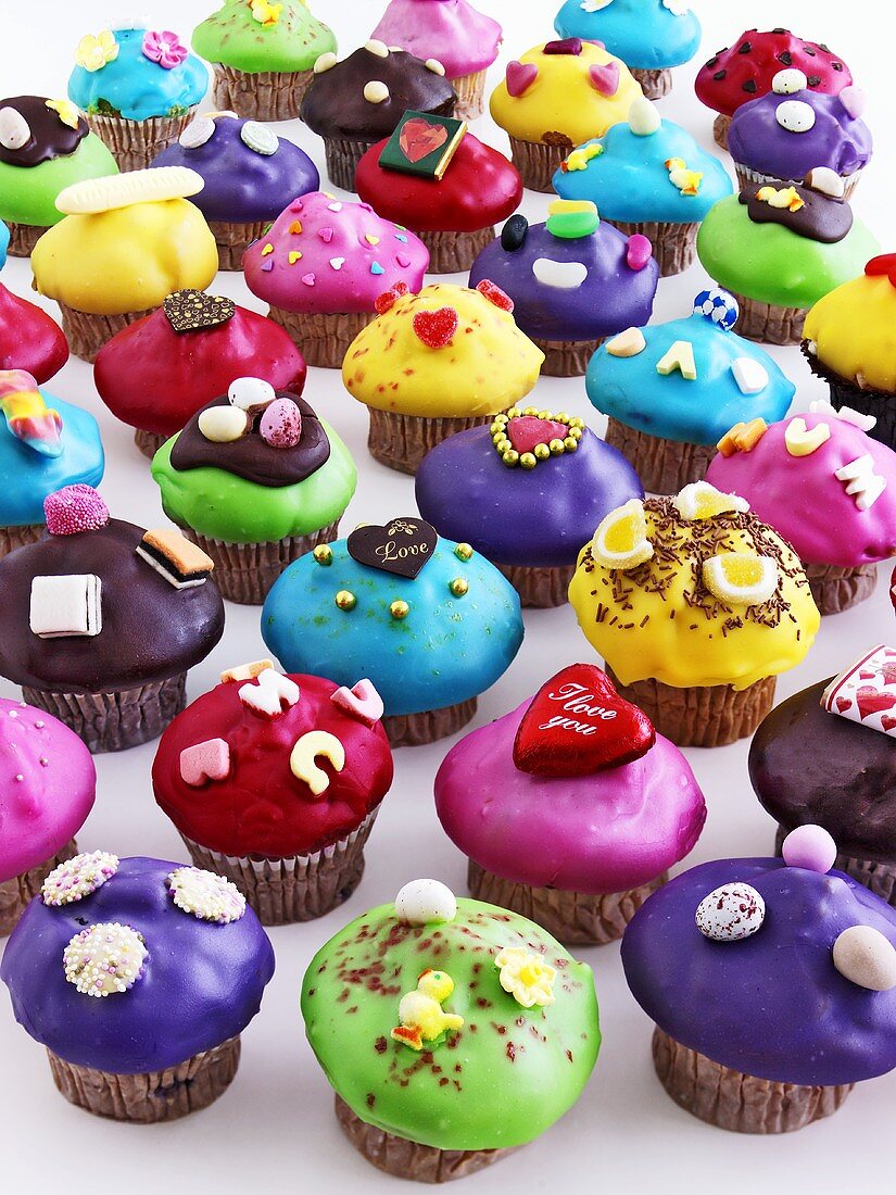 Many muffins with coloured icing and decorations