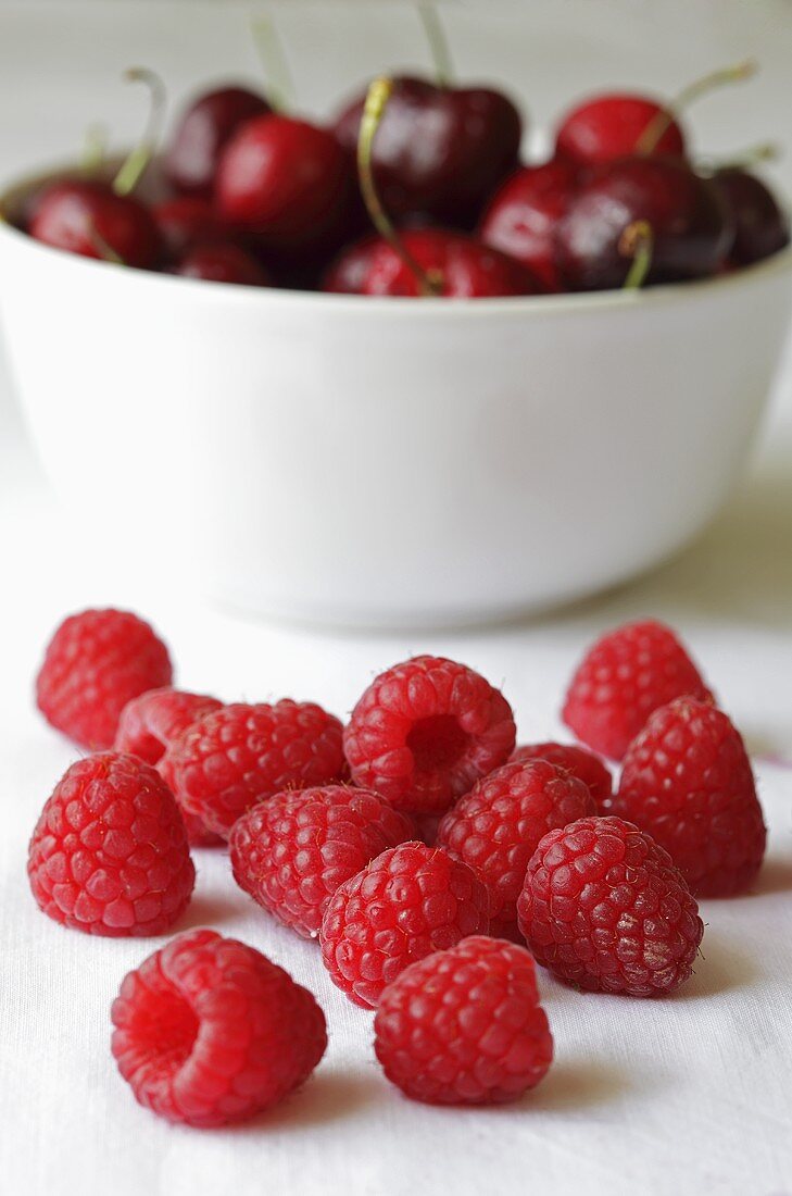 Frische Himbeeren vor einer Schale Kirschen