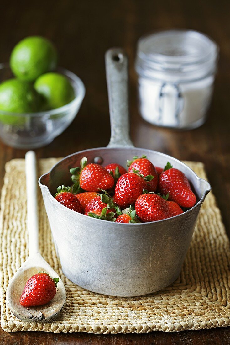 Frische Erdbeeren im Saucentopf, Limetten, Zucker