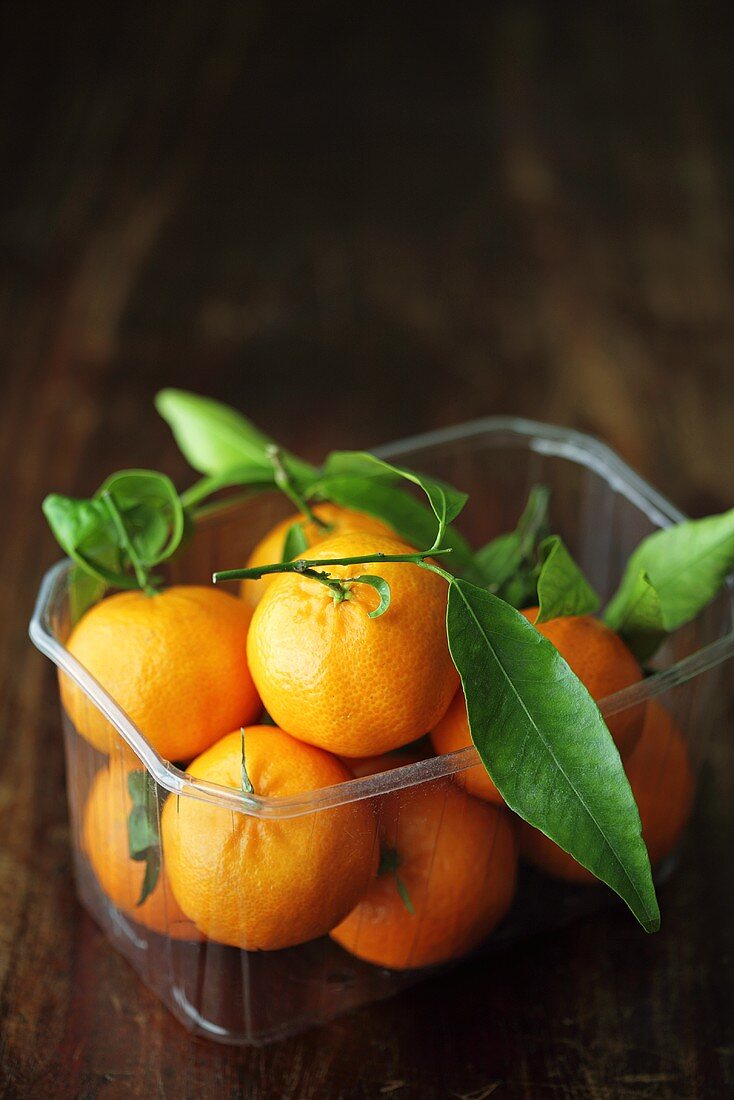 Mandarinen mit Blättern in einer Plastikschale
