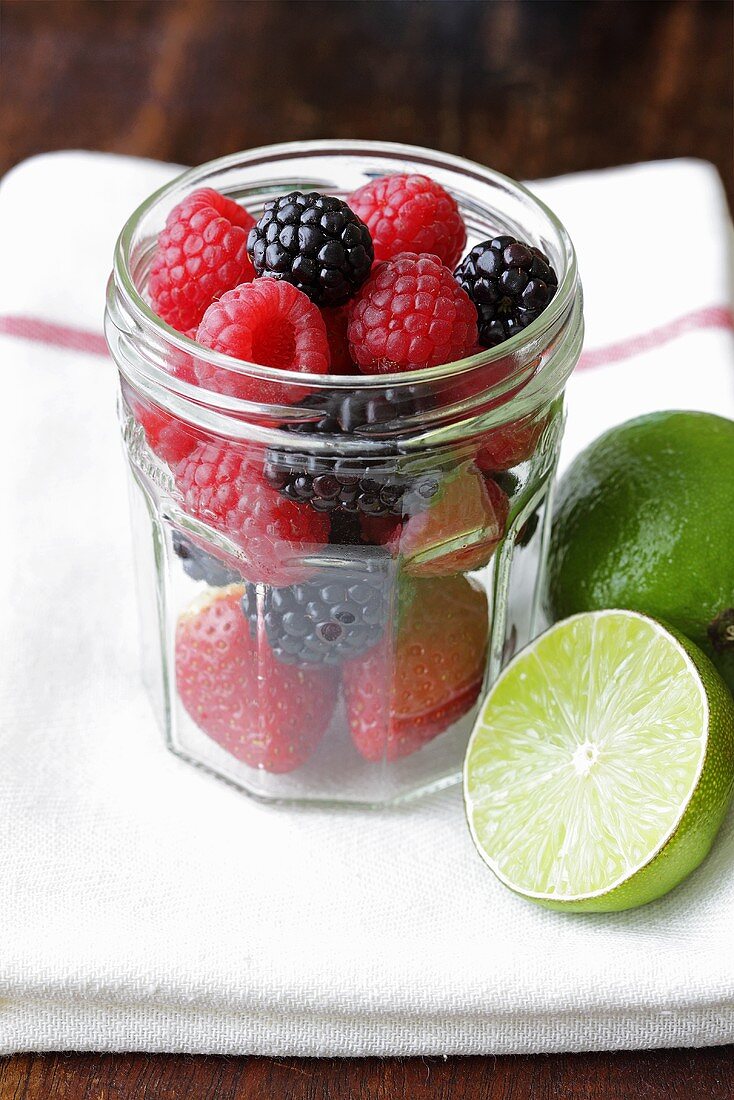 Fresh raspberries and blackberries in screw-top jar, lime