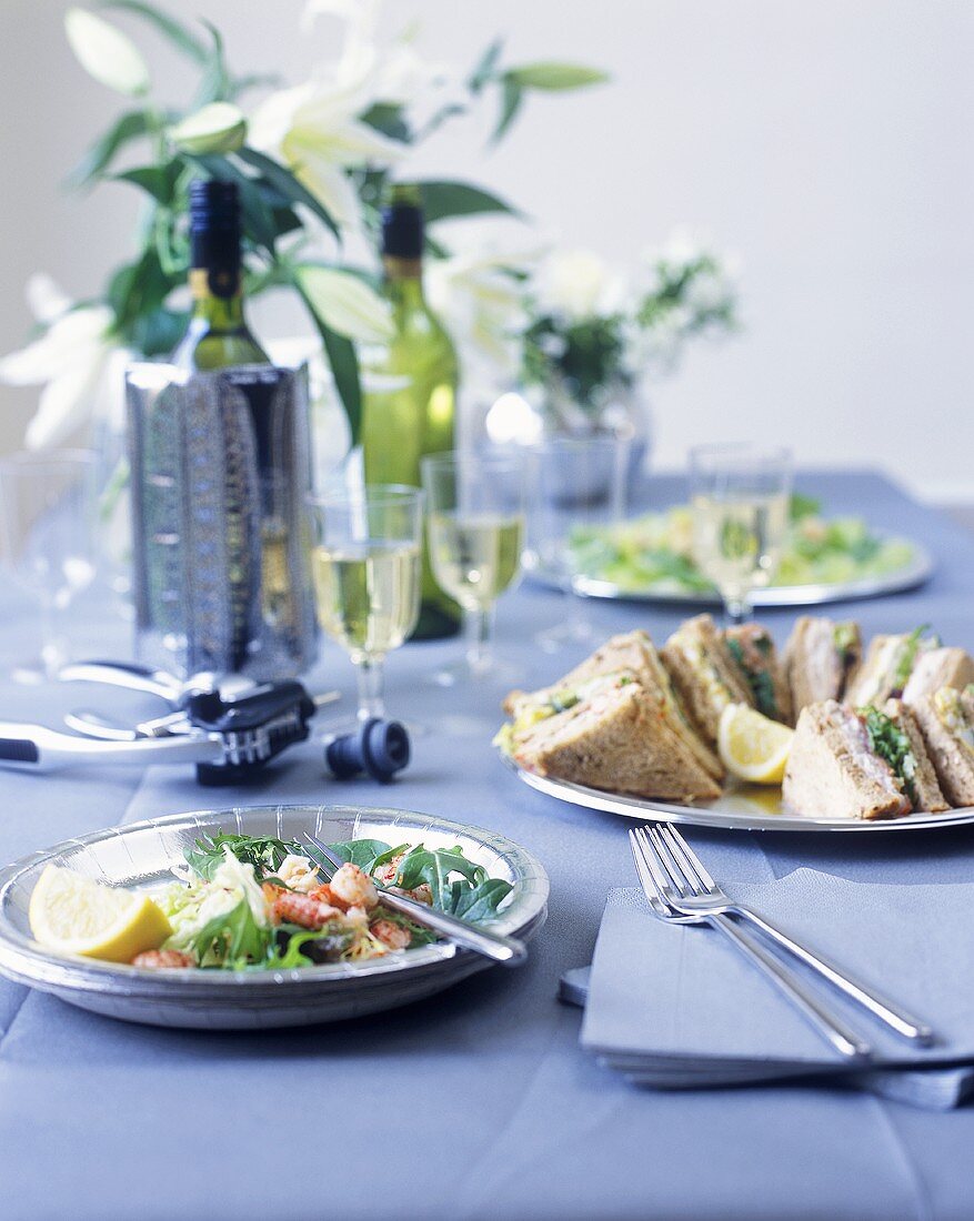Sandwiches, Salate und Wein auf blau gedecktem Partytisch