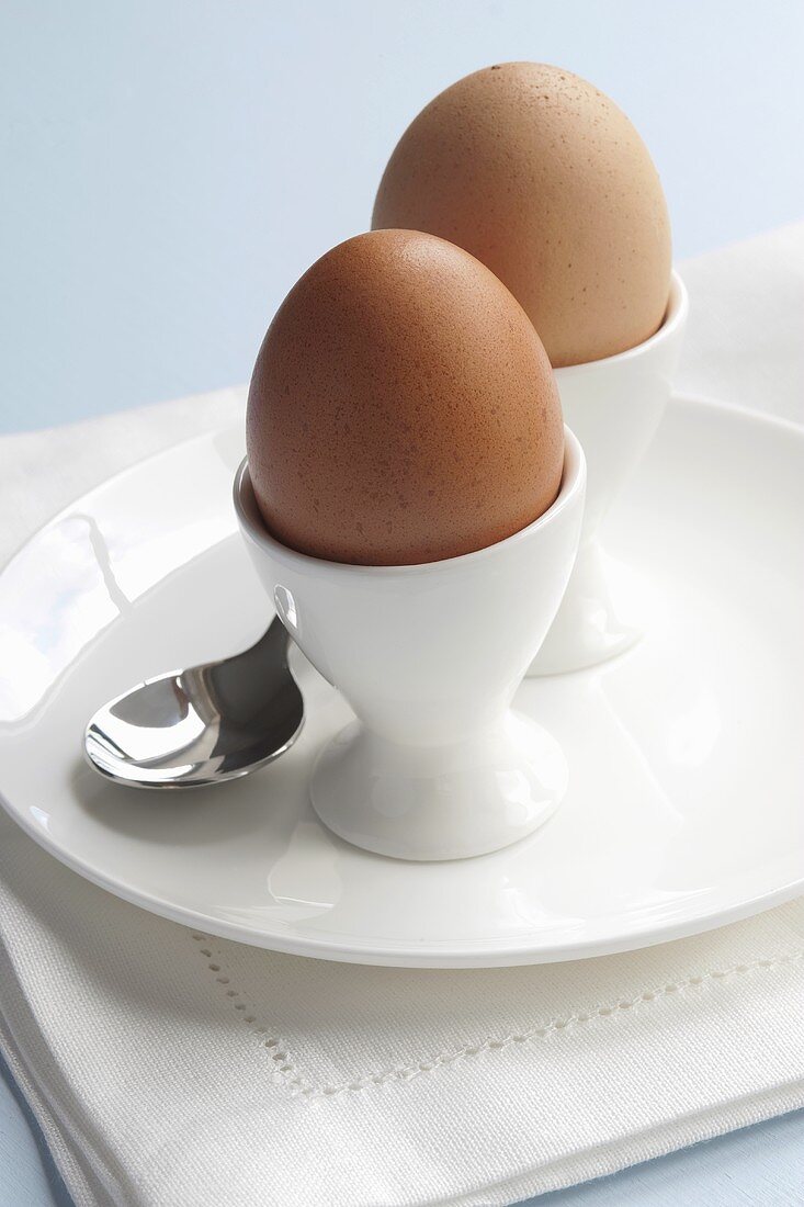 Two boiled eggs in egg cups with spoon on plate